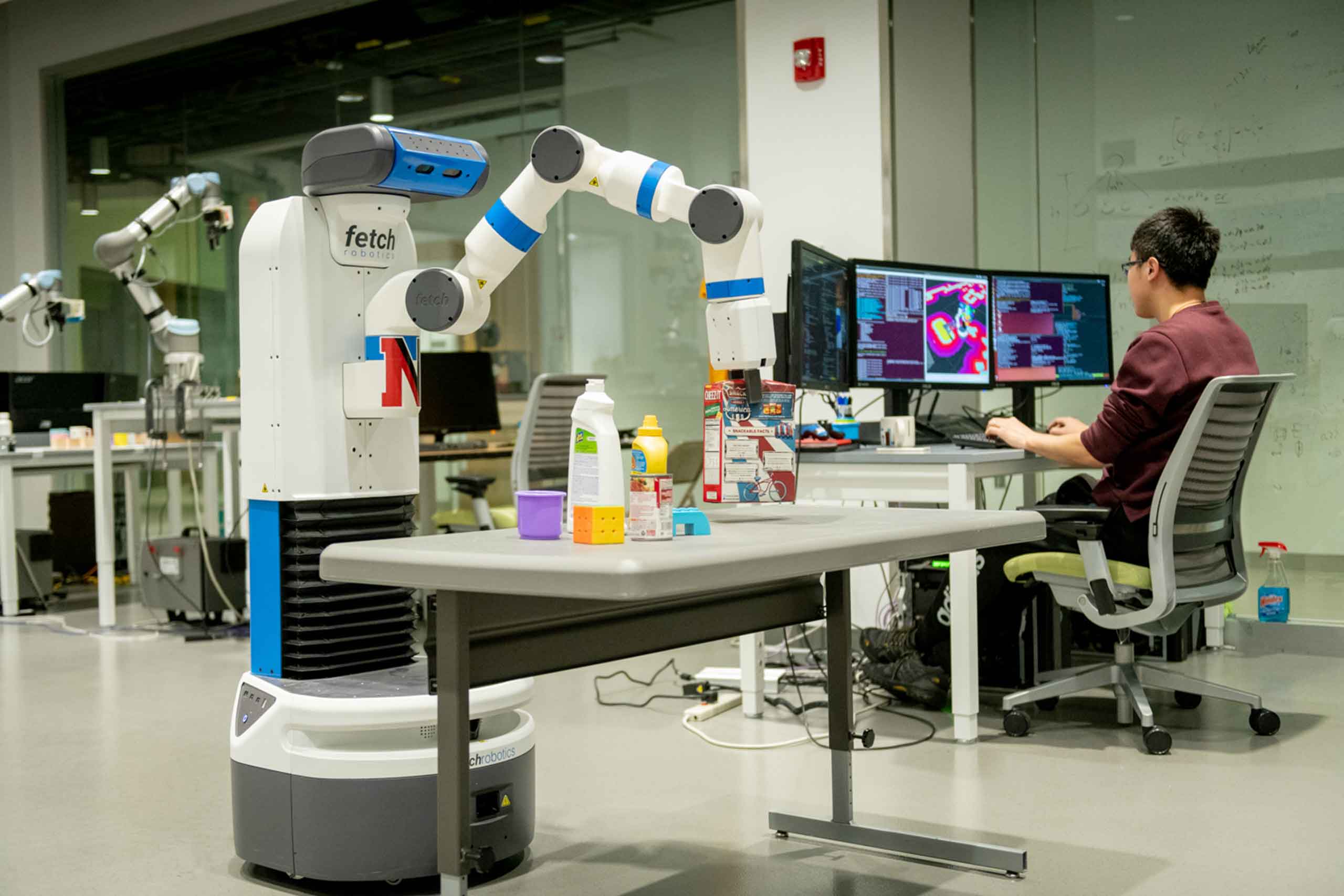 a student works at a desk in a robotics lab with a robot nearby