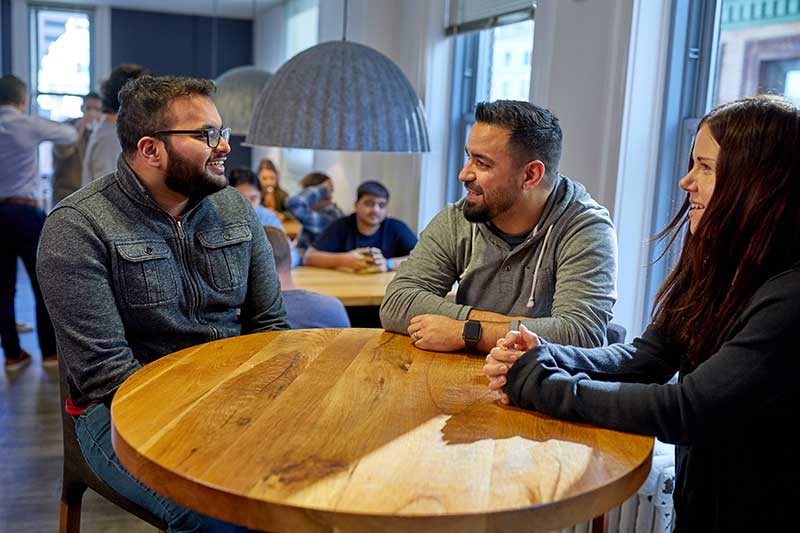 Three people talk while sitting around a table. Image of SimpliSafe engineers and staff provided by the company.