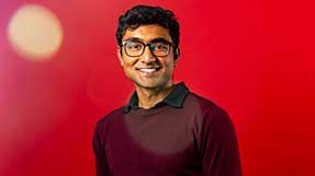 Vivek Kanpa smiles in front of a red background