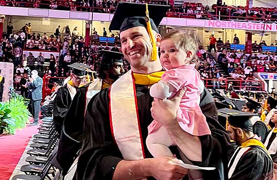 A Khoury graduate student holds his child at the graduate ceremony