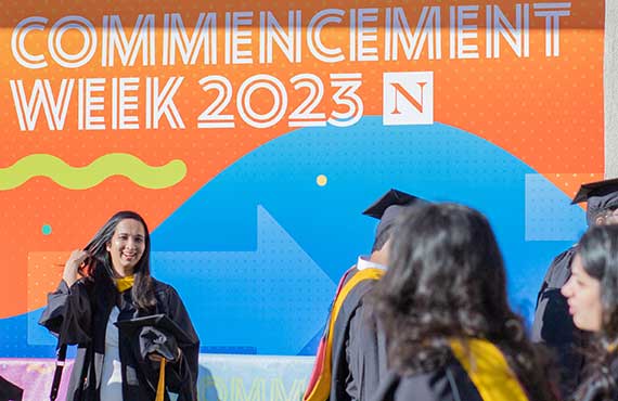 A graduate smiles in front of the Commencement Week 2023 sign