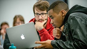 Two students view a laptop in a classroom