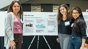 Three students stand around a poster describing a research project