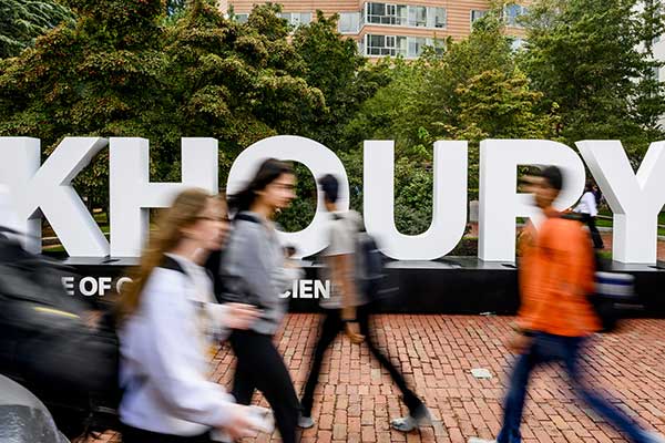 Northeastern students walk on a sidewalk with a Khoury sign in the background