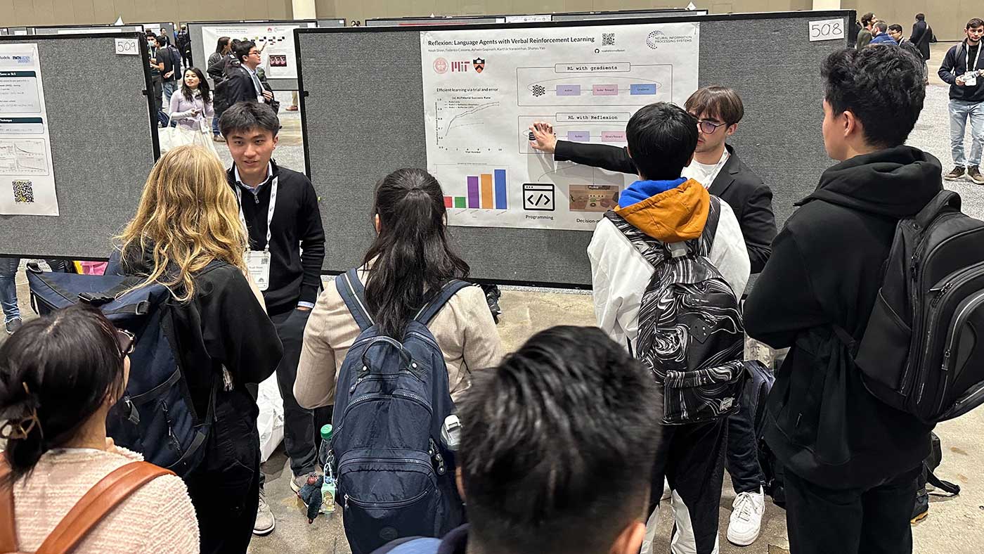 Noah Shinn and Federico Cassano present their research poster to six other students.