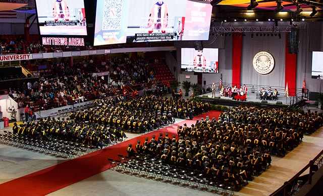 An overhead view of Northeastern's 2023 graduate ceremony showing many rows of graudates sitting in chairs while a speaker gives a speech on the podium.