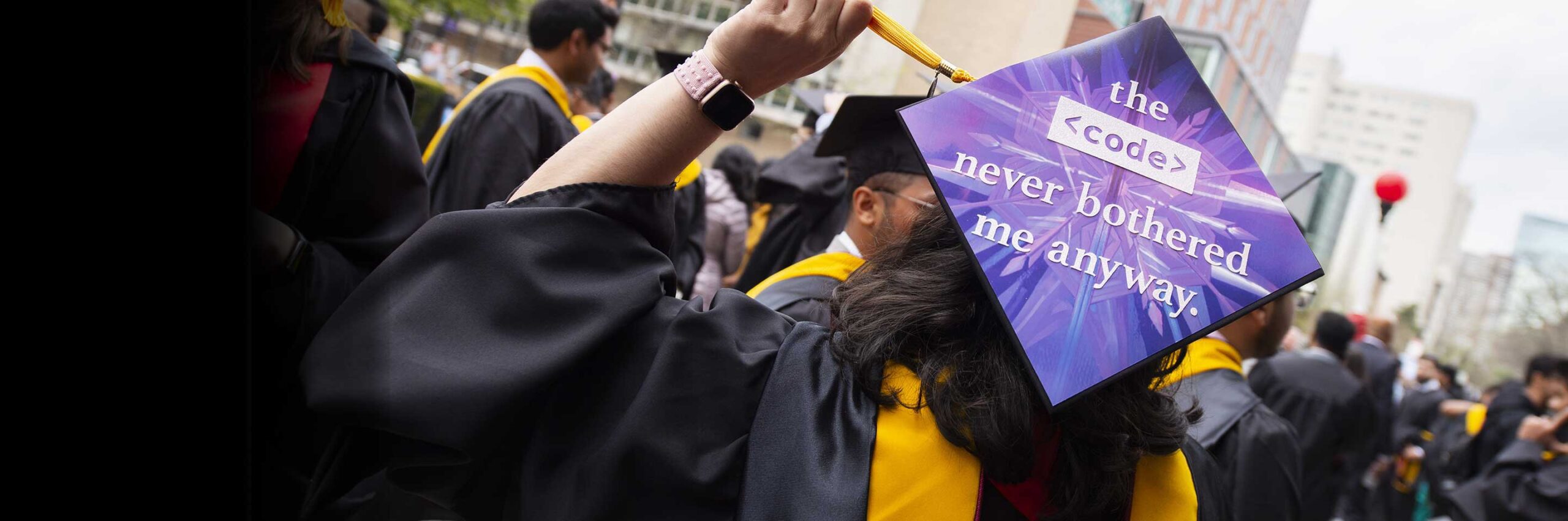 A graduate shows the back of a graduation cap with a sign that says 'the code never bothered me anyway'