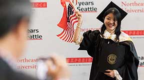 A graduate waves flags of the United States and China while holding her diploma at Commencement.
