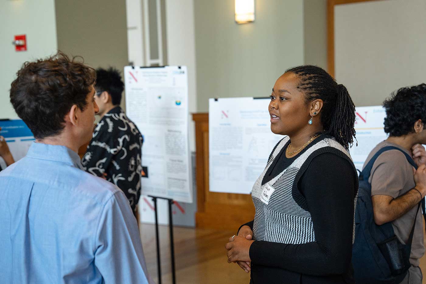Lauryn Fluellen discusses her research with another student. The two students are standing in a ballroom.