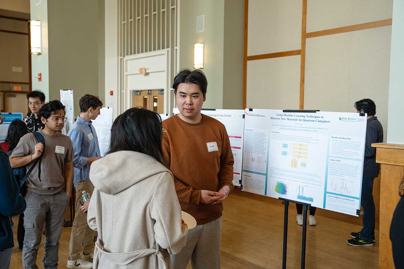 Jiawen Zou stands in front of his poster while discussing his research with another student