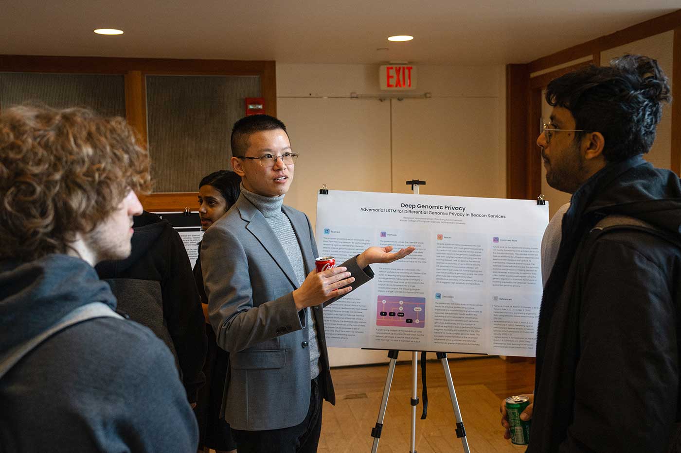 Zhou Fang stands in front of his research poster and explains his research to two other students