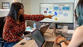 Maitraye Das (left) points at a computer screen while two other researchers look at the screen.