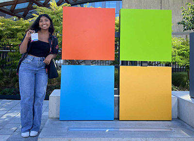 Adithi Ponakampalli smiles while holding her employee badge next to a Microsoft logo