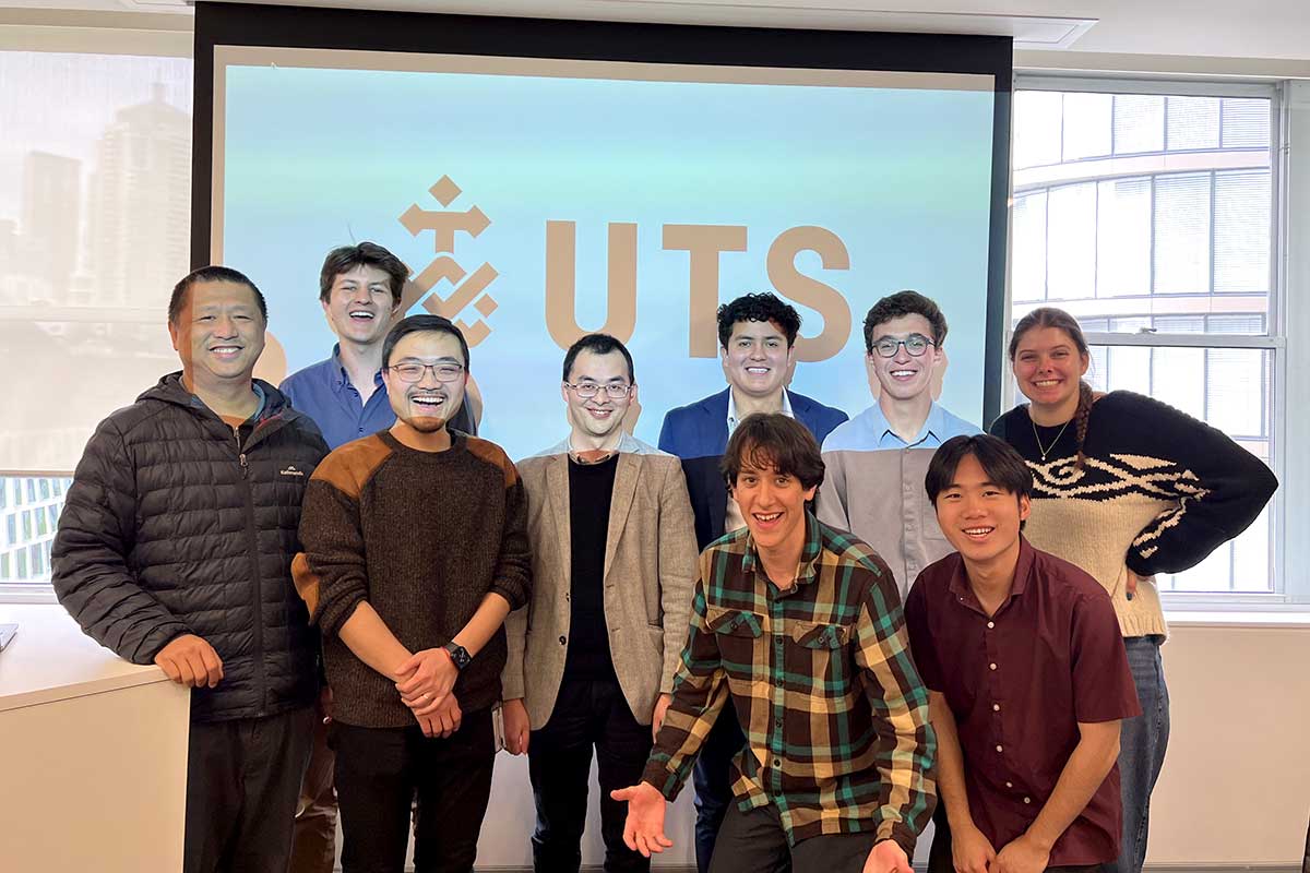 Khoury students and faculty stand in front of a projection screen that shows the letters 'UTS'