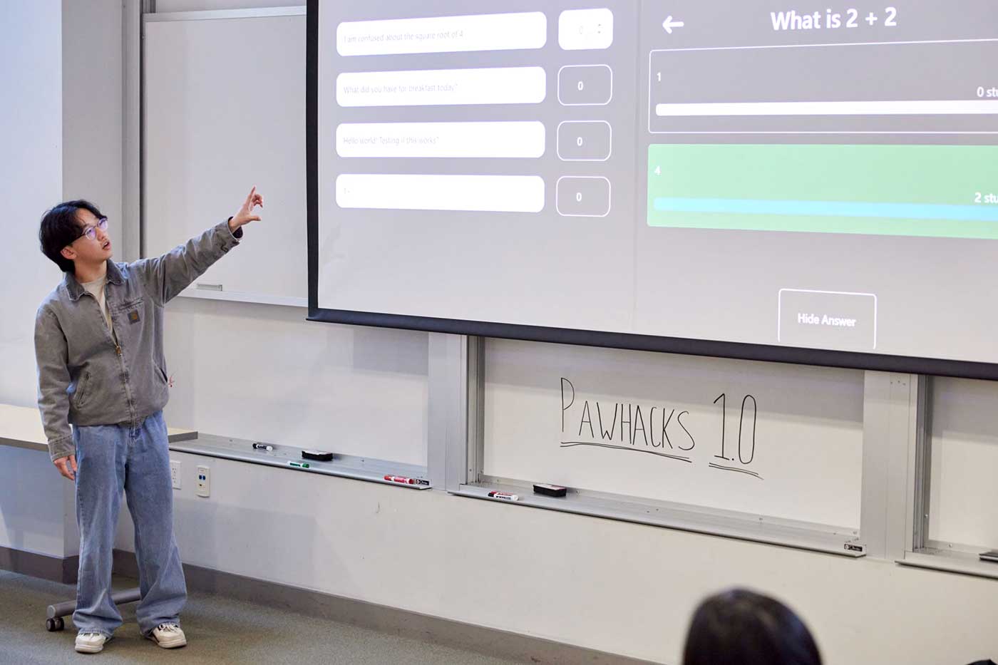 A member of the Lectura team points at a large projection screen that shows the question: What is 2 plus 2